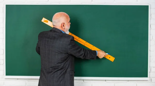 Maestro hombre mayor utilizar regla mientras dibuja. tutor barbudo dibujar con regla en pizarra. de vuelta a la escuela. disciplinas escolares. Educación y conocimiento. formas geométricas en la escuela secundaria —  Fotos de Stock