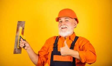 Sıva için alçı aletleri. sarı alçıpanlı alçıpanlı alçıpan spatulası. Üniformalı sıvacı, duvarları kapalı bir yerde sıva yapıyor. Spatulalı adam. Macun katmanının uygulanma süreci
