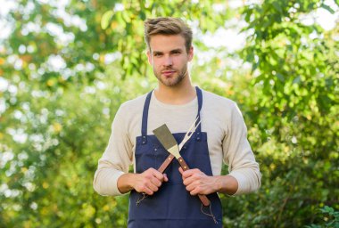Barbekü partisi. Piknik konsepti. Barbekü şefi. Yemek pişiren yakışıklı adam. Hamburger pişiriyorum. Adam barbekü malzemelerini tutuyor. Izgara yemek. Barbekü aletleri. Yaz haftasonu. Açık havada et kızartmak için araçlar