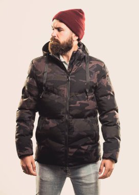 Sakallı adam beyaz arka planda izole edilmiş sıcak kamuflaj desenli ceket giyiyor. Hipster kış modası. Şapka takan ve siyah kışlık ceket giyen adam. Rahat bir kış kıyafeti. Kış stili erkek giyim