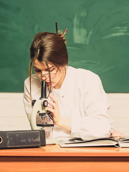 Laboratory testing. Smart student look in microscope in school laboratory. Pretty woman doing laboratory research in chemistry or biology. Supplied with new up-to-date laboratory equipment