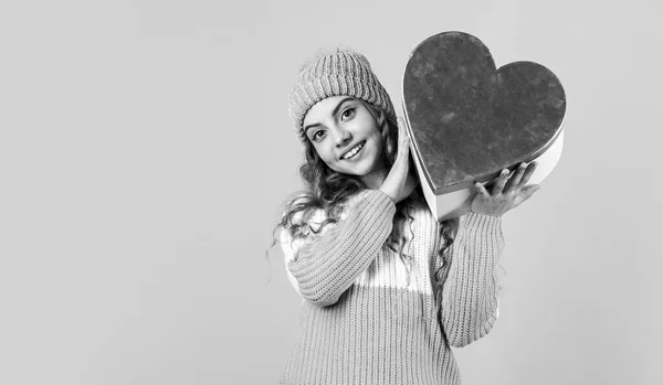 Tradición del día de San Valentín. Sé mi San Valentín. Felices fiestas de invierno. Alegre niña tejida sombrero y suéter. Niño mantenga el corazón presente caja fondo verde. idea de celebración de San Valentín. Humor romántico — Foto de Stock