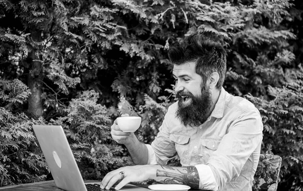 Trabalho fora do local. Hipster beber chá e usando computador estação de trabalho ao ar livre. Homem barbudo a fazer o seu trabalho online. Trabalhando globalmente através do trabalho à distância — Fotografia de Stock