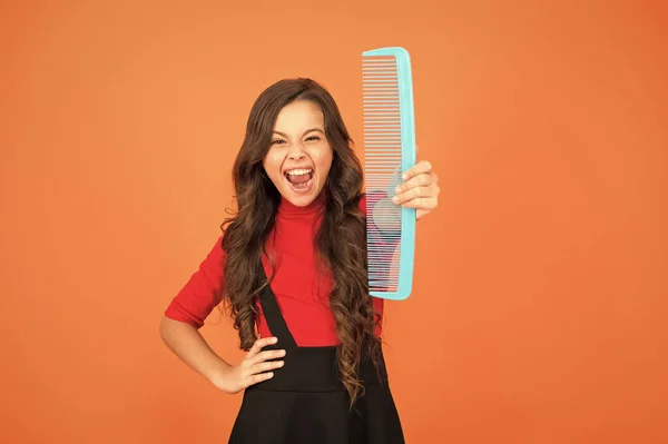 Get rid of annoying tangles. Large comb. Girl long hair hold enormous comb close up. Hairdresser salon. Combing hair. Cheerful smiling little kid with giant comb. Styling tips. Comb for tangled hair