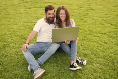 Çevrimiçi eğlence platformu. Çevrimiçi yayın hizmetlerine abone olun. Modern teknolojiler. Defterli bir çift çimenlikte oturuyor. İnternette sörf yapmak. Boş zamanlarını bilgisayar başında geçir. Ekranda bir erkek var. Çevrimiçi yaşam