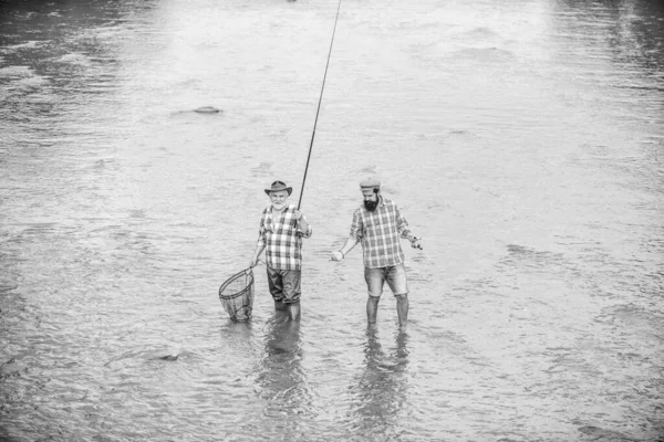 Men stand in water. Fishing is much more than fish. Happy fisherman with fishing rod and net. Hobby and sport activity. Male friendship. Father and son fishing. Summer weekend. Fishing together