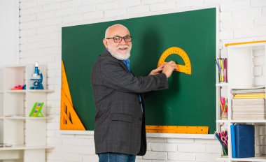 Geometriyi kolayca öğren. Matematikte iyi ol. Sınıfta kök. Kıdemli öğretmen tahtada araç kullanır. Gözlüklü sakallı öğretmen. Okula dönüyorum. İletki cetvel. Fizik ve matematik