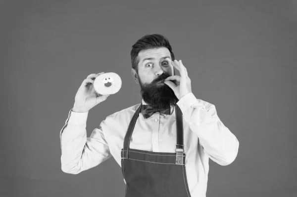Je zal je vingers likken. Bearded Man genieten van zoete smaak van donut op rode achtergrond. Baker eten donut met klassieke smaak dessert. Het smaakt goed. Kom de smaak van vreugde beleven — Stockfoto