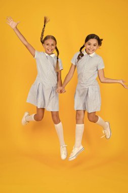 Eğleniyorum. Eski moda. Klasik tarzda çocuklar. Eski usul. Mutlu arkadaşlar sarı arka planda zıplarlar. Çocuk modası güzeli. çocukluk mutluluğu. Kardeşlik kavramı. Okul üniformalı küçük kızlar