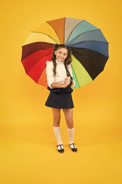Dressing cute for fall. Happy small kid going to school on rainy fall day or september 1. Little child smiling with bright umbrella for fall weather on yellow background. The right accessory for fall