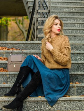 Kız eteğinin üstüne daha büyük bir katman örülmüş. Giyilebilir trendler. Sonbahar formülü. Sonbahar için Süveter ve Etek Kombo stili. Harika saç stili olan kadın merdivenlerde dışarıda oturuyor. Sonbahar moda trendi