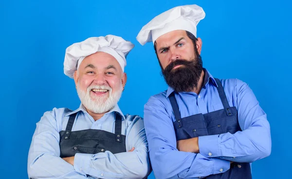 Family restaurant. Cafe workers. Restaurant kitchen. Culinary industry. Restaurant staff. Father and son culinary hobby. Mature bearded men professional restaurant cooks. Chef men wear aprons