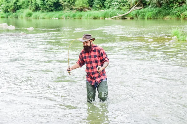 Fisher masculine hobby. Fishing requires to be mindful and fully present in moment. Fisher fishing equipment. Rest and recreation. Fish on hook. Brutal man stand in river water. Man bearded fisher