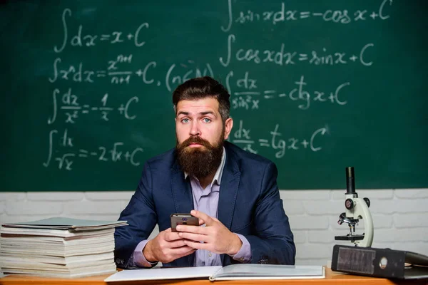 Learn technology. Modern communication. Send message. School application. Study technology. School teacher hold mobile phone chalkboard background. Teacher bearded man learn use modern technology