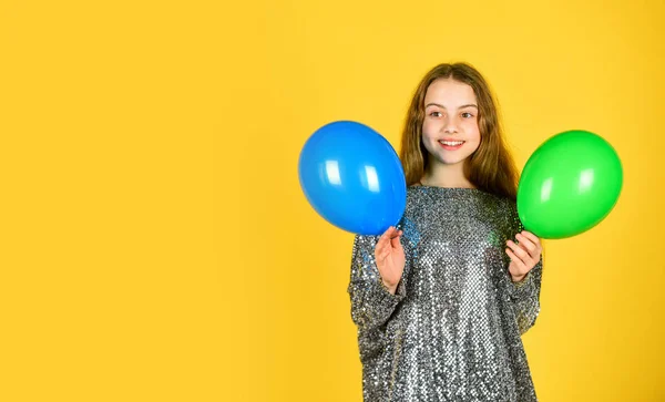 small girl hold party balloon. child wear sparkling dress yellow background. happy kid play with balloons. balloons for birthday party. colorful and bright surprise. childhood happiness. copy space