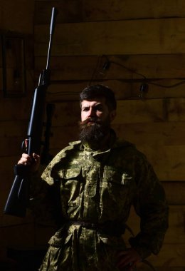 Gamekeeper 'ların evinde sert suratlı maço. Sakallı bir adam kamuflaj kıyafeti giyiyor, ahşap iç mekan. Avcı, silahlı vahşi hippi avlanmaya hazır. Avcı konsepti.