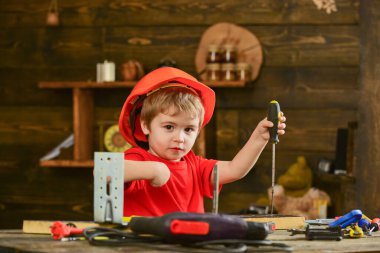 El işi ve atölye konsepti. Meşgul suratlı çocuk atölyede tornavidayla oynuyor. Miğferli çocuk inşaatçı, tamirci ya da el sanatları ustası olarak oynuyor. Çocuğun elinde tornavida aleti var..