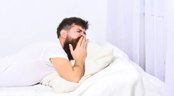 Man in shirt geeuwen tijdens het leggen op bed, witte muur en gordijn op de achtergrond. Sleepyhead concept. Macho met baard en snor geeuwen, ontspannen, een dutje doen, rusten. Man op slaperig moe gezicht geeuwt. — Stockfoto