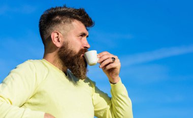 Espresso bardağıyla sakallı adam, kahve içiyor. Uzun sakallı adam kahvenin tadını çıkarıyor. Sakallı ve bıyıklı bir adam sert yüzlü kahve içiyor, mavi gökyüzü arka planda, dikkati dağılmış. Kahve gurmesi konsepti.
