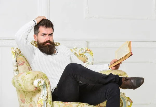 Reflections on literature concept. Connoisseur on thoughtful face finished reading book. Guy thinking about literature. Man with beard and mustache sits on armchair, holds book, white wall background. — Stock Photo, Image