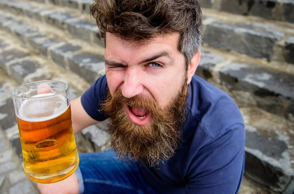 Ünnepség koncepció. Egy fickó, aki sörrel pihen. Hipster vidám kacsintós arccal sört iszik a szabadban. A szakállas és bajszos férfi üveget tart sörrel, miközben a kőlépcsőn ül, kiütve.. — Stock Fotó