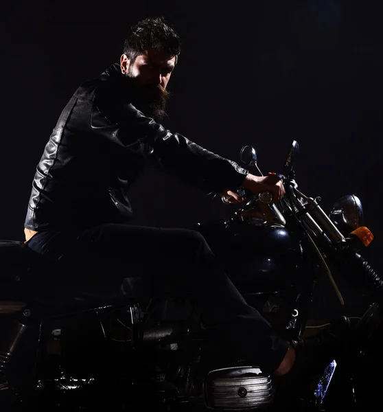 Bikers fritid koncept. Macho, brutal biker i läder jacka Rider motorcykel nattetid, kopia utrymme. Mannen med skägg, biker i skinnjacka sitter på motorcykel i mörker, svart bakgrund. — Stockfoto