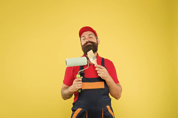 Man bearded laborer painting. Repair and renovation. Builder regular worker hold paint roller and brush. Perfect surface painting. Apply vinyl paint. Pick tools. Painting tool. Brush roller painter