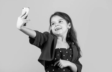 Selfie zamanı. Küçük kız, akıllı telefon sarı arka planlı selfie çekiyor. Cep telefonundaki küçük çocuk selfie kamerası. Moda tarzında selfie çekmenin tadını çıkarıyorum. İletişim çevrimiçi. Sosyal ağ