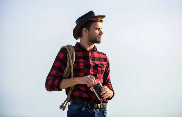 Looking for adventures. Farmer cowboy handsome man relaxing after hard working day at ranch. Lonely farmer sky background. Rustic style. Hero of western culture. Farmer drink water metal flask — Stock Photo, Image