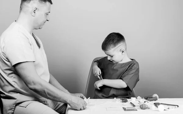 귀여운 소년 과 그 의 아버지 의사. 의학적 도움. 의료 보험. 의학적 개념. 꼬마 의사는 테이블 의료 도구를 놓고 앉아 있습니다. 건강 관리. 건강 검진. 병원 직원들의 봉급 — 스톡 사진