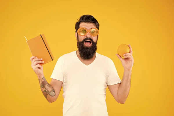 Creare una dieta di lettura equilibrata. Hipster con frutta arancione e libro per la lettura su sfondo giallo. Uomo barbuto in occhiali da lettura fantasia con la bocca aperta. Continua a leggere — Foto Stock