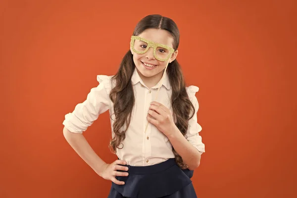 O que significa ser inteligente? Uma estudante esperta no fundo laranja. Criança pequena usando óculos em estilo inteligente. Conceito de festa escolar. Criança olhar inteligente através de óculos de suportes de cabine de fotos — Fotografia de Stock