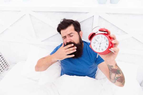 ¿Por qué sufres por las mañanas? Levántate con el despertador. Me levanté temprano. Hombre barbudo somnoliento cara cama con despertador en la cama. Un ruido terrible. Apaga el timbre. Problema de despertar temprano en la mañana — Foto de Stock