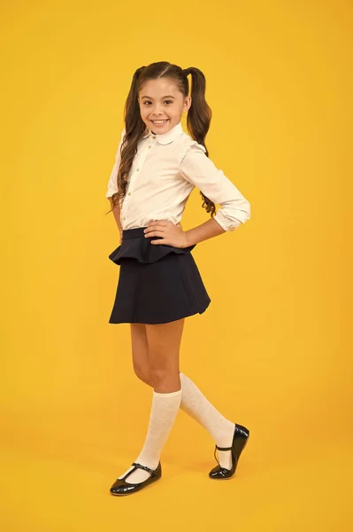 Μοντέρνο και αριστοκρατικό. Μικρό κορίτσι με μακριά μαλλιά χαμογελώντας σε μοντέρνα σχολική στολή. Ευτυχισμένο σχολείο με μοδάτο βλέμμα σε κίτρινο φόντο. Μόδα πίσω στις σχολικές τάσεις — Φωτογραφία Αρχείου