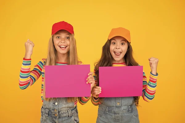 A tua publicidade ganha. Crianças pequenas felizes mostrando folhas de papel rosa para publicidade em fundo amarelo. Menina publicidade produto ou evento. Ganhar soluções de publicidade para você, espaço de cópia — Fotografia de Stock