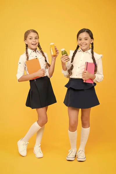 Thirst and dehydration. Healthy snack fruit smoothie. Smoothie detox. Yummy smoothie. Healthy nutrition. Schoolgirls holding juice bottle on yellow background. Quenching thirst during school time — Stock Photo, Image