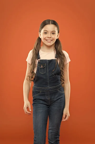 Feliz infancia. Crecer niño mental y físicamente saludable. Bienestar y salud. Concepto de infancia. Chica de moda. Niña adorable niño de pie sobre fondo naranja. ¿Cuál es la clave de la felicidad infantil? —  Fotos de Stock