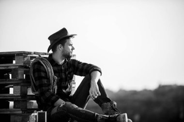 Çiftçi kovboy yakışıklı adam çiftlikte sıkı çalıştıktan sonra dinleniyor. Çiftçi çiftliğinin manzarasının tadını çıkarıyor. Batı kültürünün romantizmi. Şapkalı çiftçi rahatına bak. Huzurlu bir ruh hali. Gün batımını izlerken