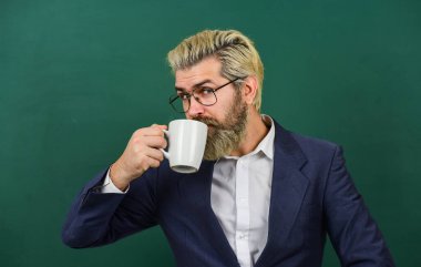 Hoş bir yudum. Kahve molası ve rahatla. Öğretmen için öğle yemeği zamanı. Kahve bağımlısı. Tüm gün boyunca enerji yüklenmesi. Bir doz kafein. İyimserlik kavramı. Gözlüklü öğretmen kahve tahtası arkaplanı içer.