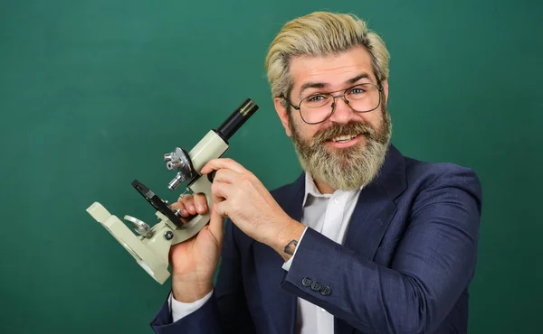 Insegnante che cerca microscopio. Ricerca scientifica. Ricerca affascinante. Insegnante con microscopio. Uomo hipster classe lavagna sfondo. Ricerca biologica. Facilitare il progresso accademico — Foto Stock