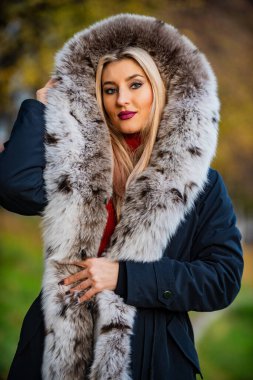 Gerçekten sıcak ve samimi. Pahalı kıyafetler. Lüks segment markası. Lüks kürk. Güzellik ve moda. Kadın kürklü kapüşonlu bir ceket giyiyor. Sahte kürk kumaşı. Sonbahar parkında zarif bir kız yürüyor. Kürk giysiler
