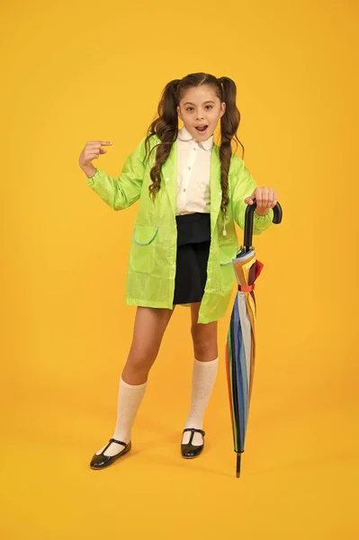 C'est une victime de la mode. Mignon écolier pointant du doigt avec look de mode sur fond jaune. Petit enfant en imperméable tenant parapluie de mode. Mode pluie et jour de pluie — Photo