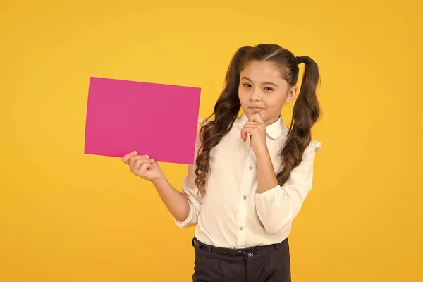 Pour des informations scolaires. Petit enfant tenant du papier rose vide pour information sur fond jaune. Petite fille avec avis d'information. Diffuser l'information et recueillir des connaissances, copier l'espace — Photo