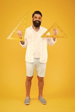 Burada üçgenleri öğrenmek kolaydır. Sarı arka planda üçgenler tutan mutlu sakallı adam. Okul öğretmeni veya öğrenci geometri dersi için geometrik üçgenler ile gülümseyen. Üçgenlerde ders