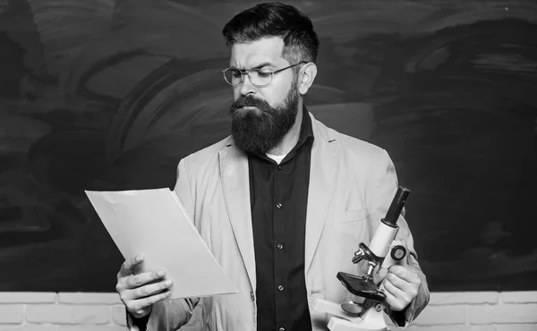 Teacher bearded man hold documents and microscope chalkboard background. Explaining theory. College and high school. Prepare for test. Biology is his passion. Demanding teacher. Lecturer in classroom — Stock Photo, Image