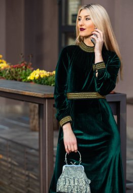Seçimine güveniyor. Seksi iş kadını dışarıda telefonda konuşuyor. Modern hayat. Kız mücevher çanta ya da çanta. Glam debriyaj aksesuarı. Yeşil kadife elbiseli zarif bir kadın. cazibe kadife tekstil