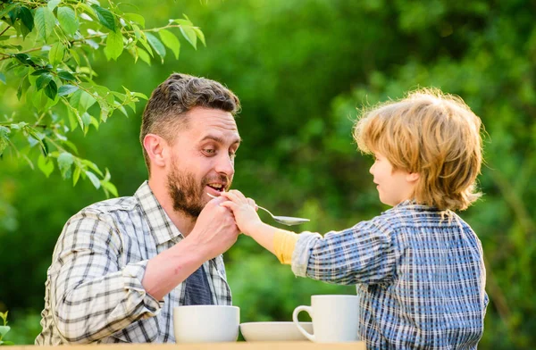 Nakarm swoje dziecko. Naturalne odżywianie. Karmienie syna naturalną żywnością. Etap rozwoju. Nakarm syna na stałe. Tata i syn jedzą i karmią się nawzajem na dworze. Sposoby rozwijania zdrowych nawyków żywieniowych — Zdjęcie stockowe