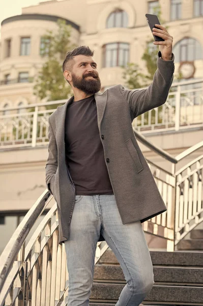 Ruční selfie. Vousatý muž vzít selfie s chytrým telefonem venku. Podnikatel se usměje na selfie kameru v mobilním telefonu. Užívá si selfie session v obchodním stylu. Moderní život — Stock fotografie