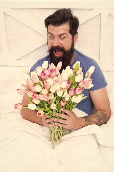 Springtime. good morning flowers. positive mood and happiness. surprised bearded man in bed. birthday gift bouquet. spring fresh tulip. love valentines day. womens day. tulip flower for march 8