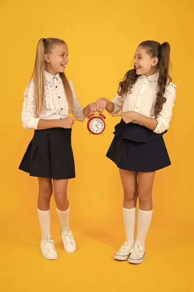 Keep your students safe and on time. Happy little girls holding retro clock during school time on yellow background. Small child holding alarm clock. Time to learn. School clock and time solution